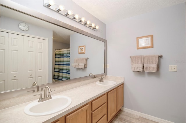 full bathroom with a sink, baseboards, a textured ceiling, and double vanity