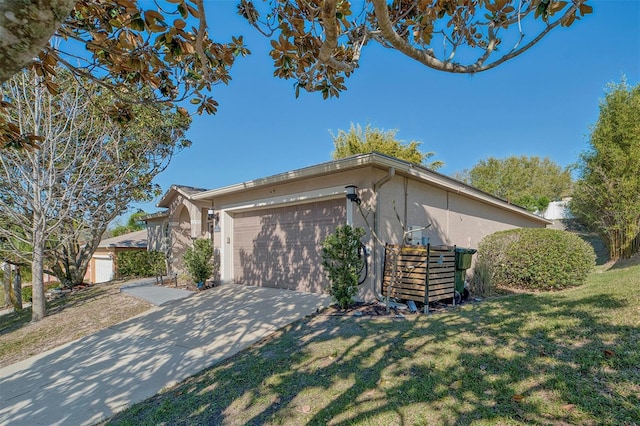 view of side of property featuring stucco siding, driveway, a lawn, and a garage