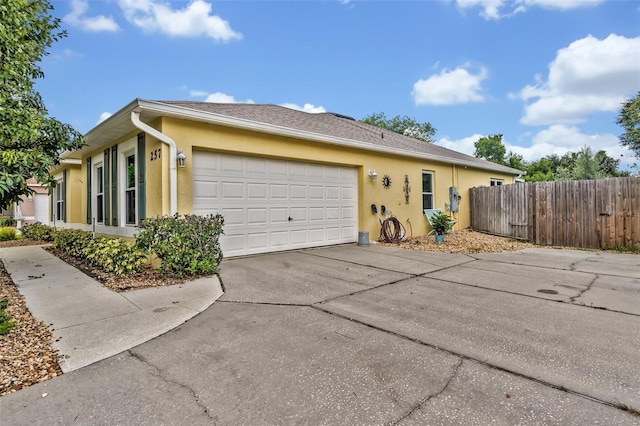 view of front of home featuring stucco siding, fence, roof with shingles, concrete driveway, and an attached garage