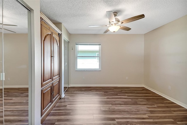 unfurnished bedroom featuring ceiling fan, a textured ceiling, dark wood-type flooring, and baseboards