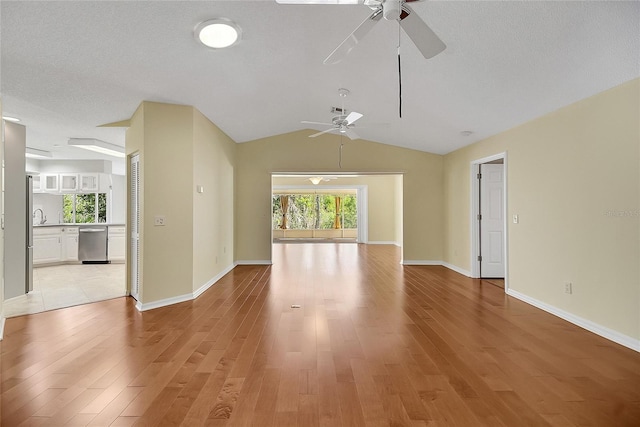 spare room with lofted ceiling, light wood-style flooring, a textured ceiling, baseboards, and ceiling fan