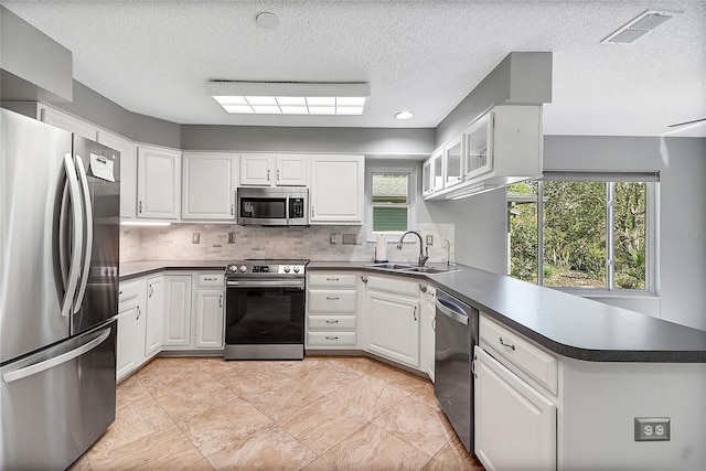 kitchen featuring dark countertops, visible vents, appliances with stainless steel finishes, a peninsula, and a sink