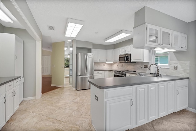 kitchen with a sink, tasteful backsplash, appliances with stainless steel finishes, white cabinets, and a peninsula