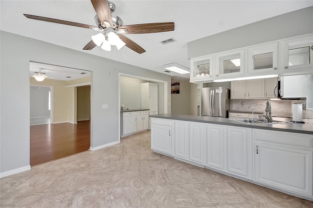 kitchen featuring dark countertops, visible vents, glass insert cabinets, freestanding refrigerator, and a sink