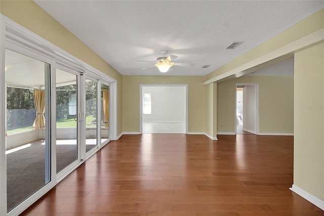 unfurnished room with visible vents, a textured ceiling, wood finished floors, baseboards, and ceiling fan