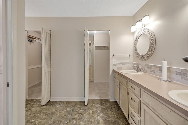 bathroom with tasteful backsplash, baseboards, double vanity, a textured ceiling, and a sink