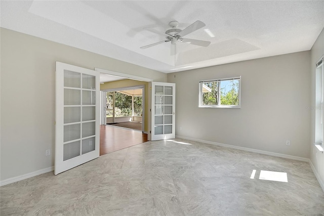 unfurnished room with plenty of natural light, a ceiling fan, a raised ceiling, and baseboards