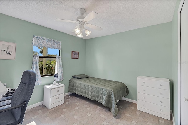 bedroom with a textured ceiling, a ceiling fan, brick floor, and baseboards