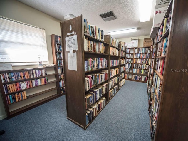 interior space with bookshelves, visible vents, carpet flooring, and a textured ceiling