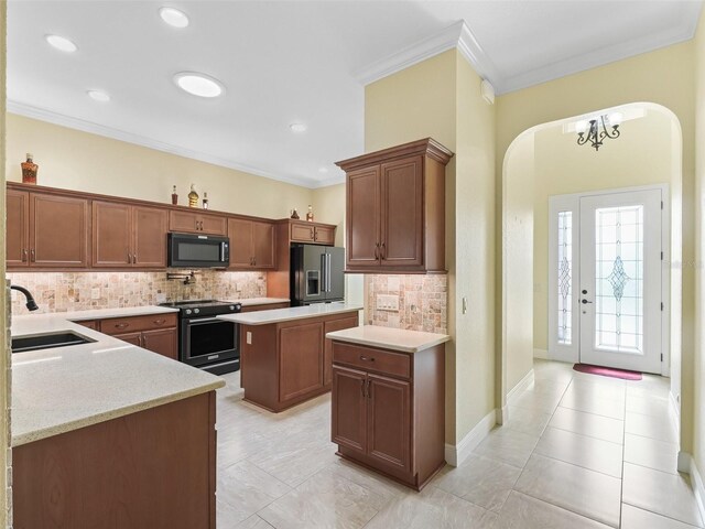 kitchen with tasteful backsplash, crown molding, black appliances, arched walkways, and a sink