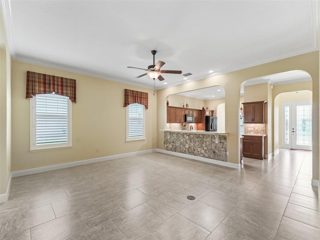 unfurnished living room featuring crown molding, ceiling fan, and arched walkways