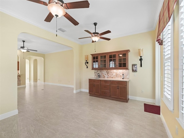 interior space featuring ceiling fan, arched walkways, ornamental molding, visible vents, and baseboards