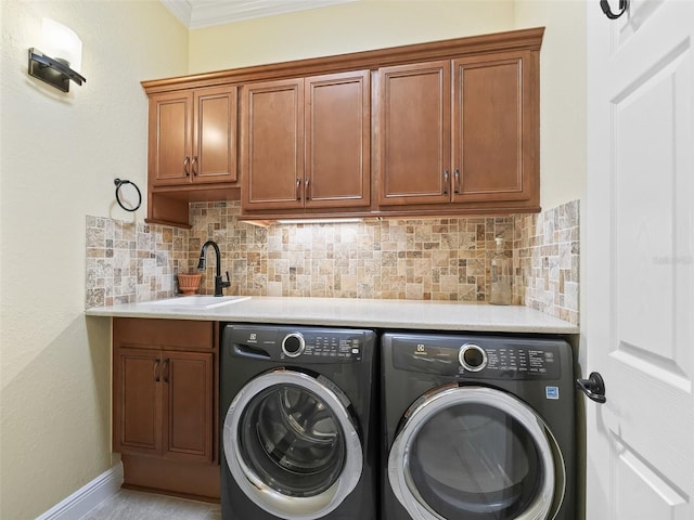 laundry room featuring baseboards, ornamental molding, cabinet space, washer and dryer, and a sink