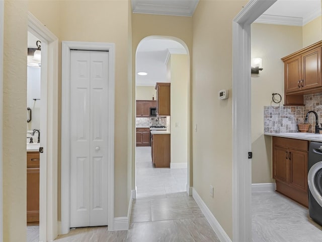 corridor featuring washer / clothes dryer, crown molding, arched walkways, marble finish floor, and a sink