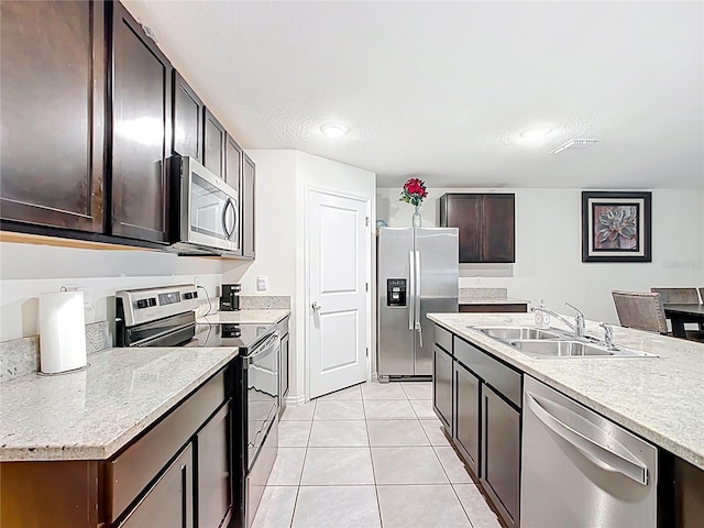 kitchen featuring dark brown cabinetry, light countertops, appliances with stainless steel finishes, light tile patterned flooring, and a sink