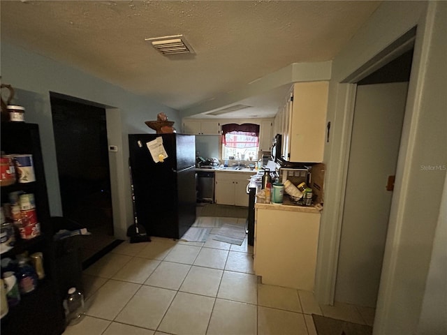 kitchen featuring visible vents, dishwashing machine, freestanding refrigerator, light tile patterned flooring, and white cabinets