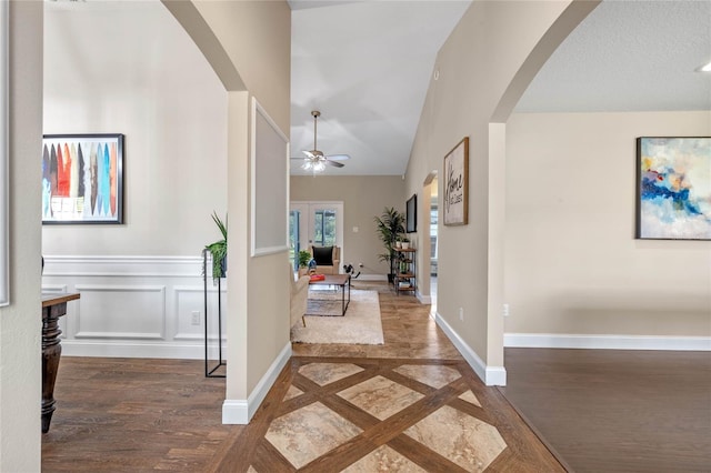 corridor featuring arched walkways, lofted ceiling, baseboards, and wood finished floors