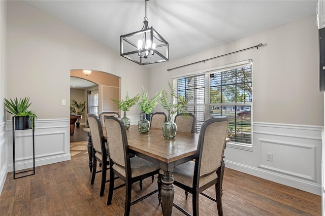 dining area with a notable chandelier, dark wood-style floors, arched walkways, and wainscoting