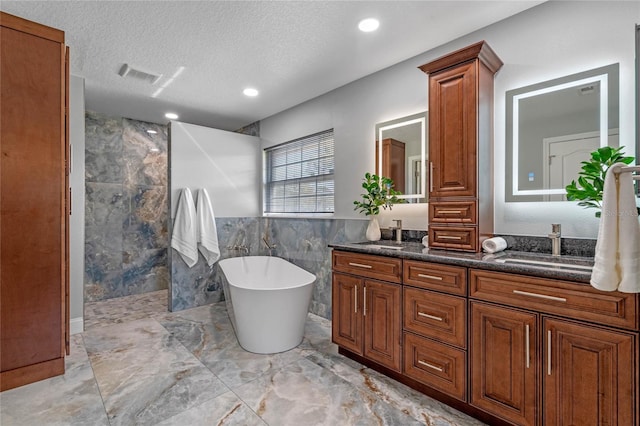 bathroom featuring visible vents, a walk in shower, a sink, a textured ceiling, and a freestanding bath