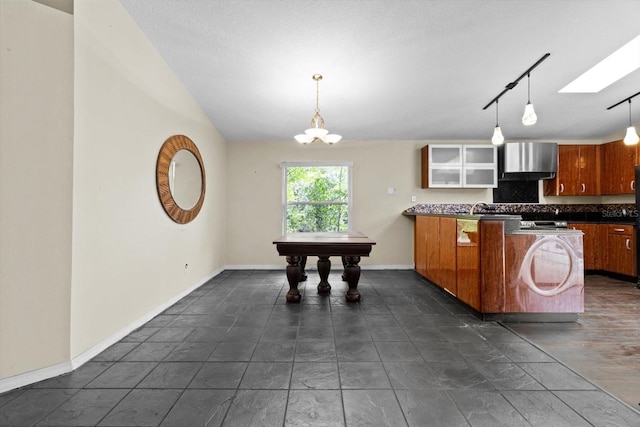 kitchen featuring brown cabinetry, a peninsula, a skylight, dark countertops, and tasteful backsplash