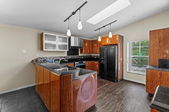 kitchen with brown cabinetry, a peninsula, wall chimney exhaust hood, backsplash, and black fridge