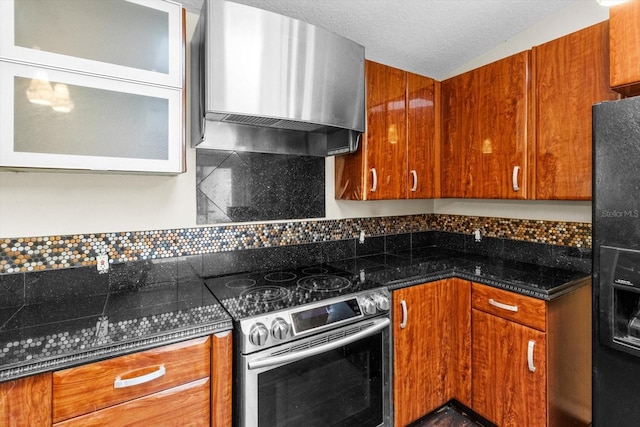 kitchen featuring brown cabinets, black fridge, tasteful backsplash, stainless steel electric range, and wall chimney exhaust hood