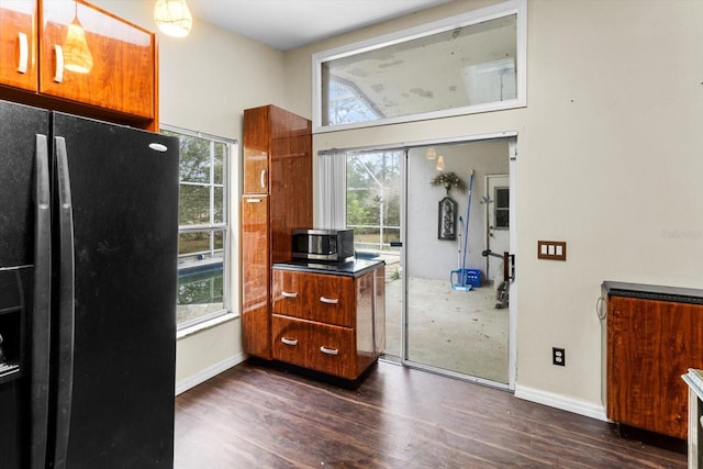 kitchen featuring dark wood finished floors, stainless steel microwave, brown cabinetry, and black fridge with ice dispenser