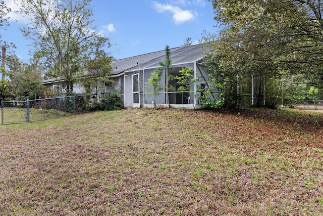 rear view of house featuring a lanai, a gate, fence, and a lawn