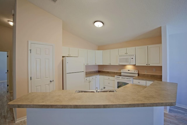 kitchen with white appliances, wood finished floors, a sink, vaulted ceiling, and white cabinetry