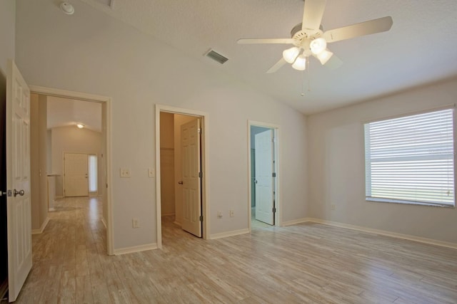 unfurnished bedroom featuring light wood-type flooring, a walk in closet, ensuite bath, baseboards, and vaulted ceiling