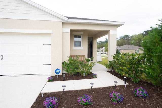 entrance to property featuring a garage, covered porch, and stucco siding