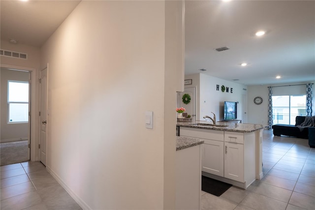 kitchen with a sink, visible vents, light stone counters, and white cabinetry