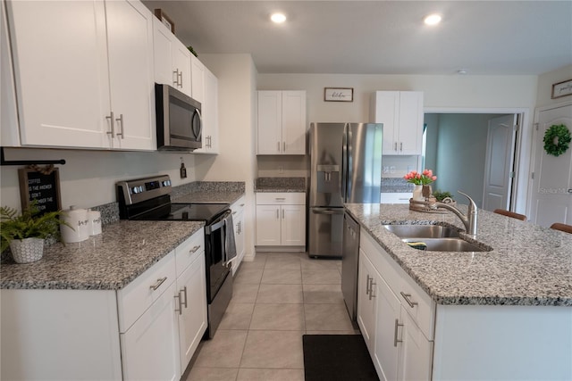 kitchen with a center island with sink, a sink, appliances with stainless steel finishes, white cabinets, and light tile patterned floors