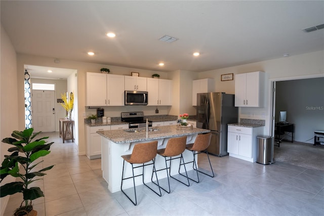 kitchen featuring visible vents, a center island with sink, appliances with stainless steel finishes, and a kitchen bar