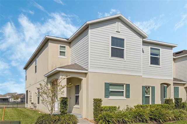 view of front facade featuring stucco siding, a front yard, and fence