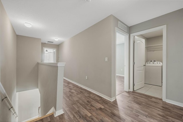 corridor featuring wood finished floors, visible vents, baseboards, washer / dryer, and an upstairs landing