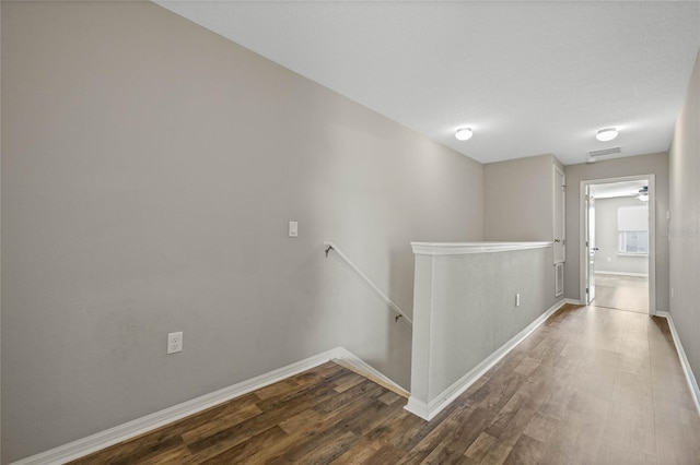 hallway with an upstairs landing, visible vents, dark wood finished floors, and baseboards