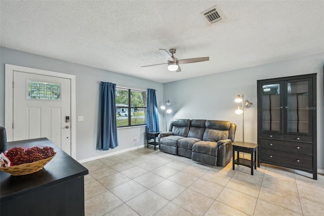 living area with visible vents, a textured ceiling, light tile patterned floors, baseboards, and ceiling fan