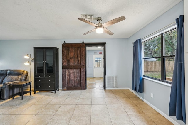 empty room featuring baseboards, visible vents, light tile patterned flooring, ceiling fan, and a barn door