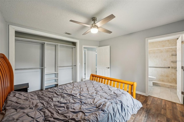 bedroom featuring wood finished floors, visible vents, a closet, a textured ceiling, and connected bathroom