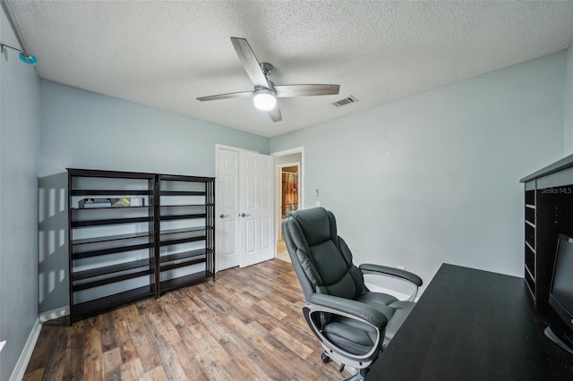 home office with visible vents, a textured ceiling, a ceiling fan, and wood finished floors