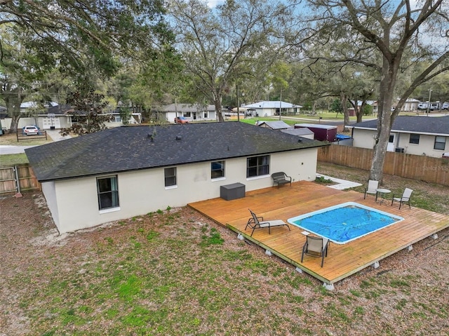 rear view of house with a fenced in pool, a wooden deck, roof with shingles, stucco siding, and a fenced backyard