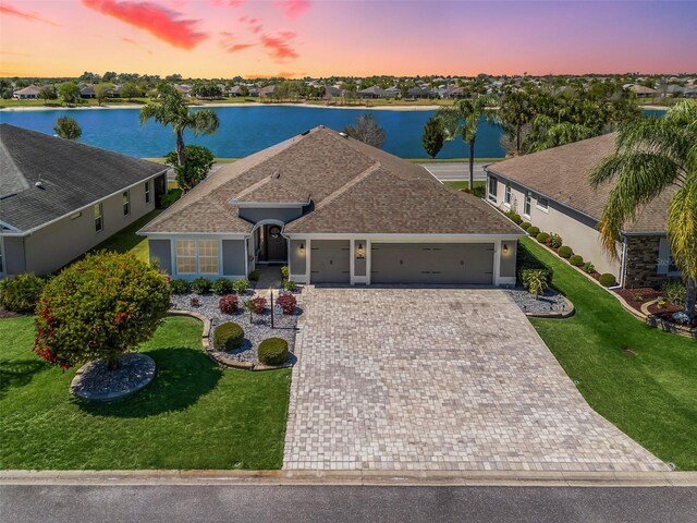 ranch-style house featuring a water view, roof with shingles, driveway, a yard, and an attached garage