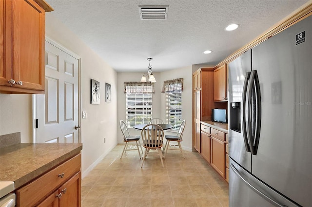 kitchen with visible vents, decorative light fixtures, brown cabinetry, stainless steel fridge, and a textured ceiling