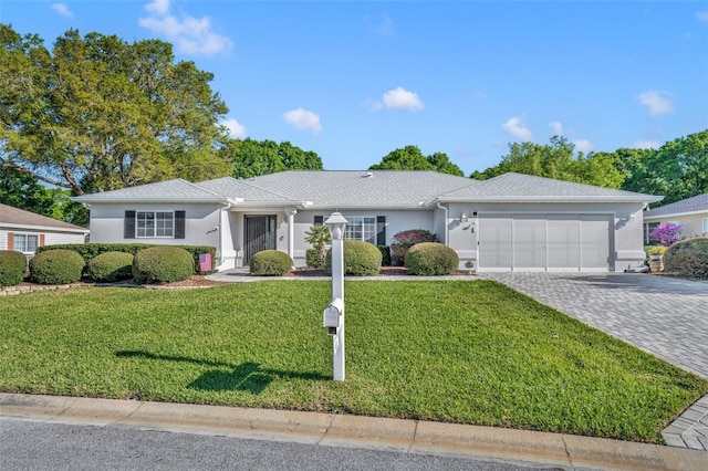 ranch-style house with a front yard, decorative driveway, an attached garage, and stucco siding