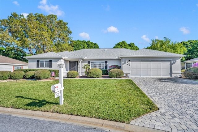 single story home featuring decorative driveway, a garage, a front yard, and stucco siding