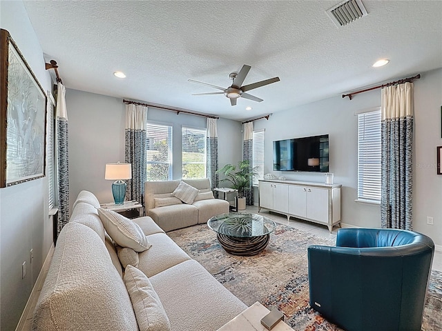 living room with a ceiling fan, visible vents, baseboards, recessed lighting, and a textured ceiling