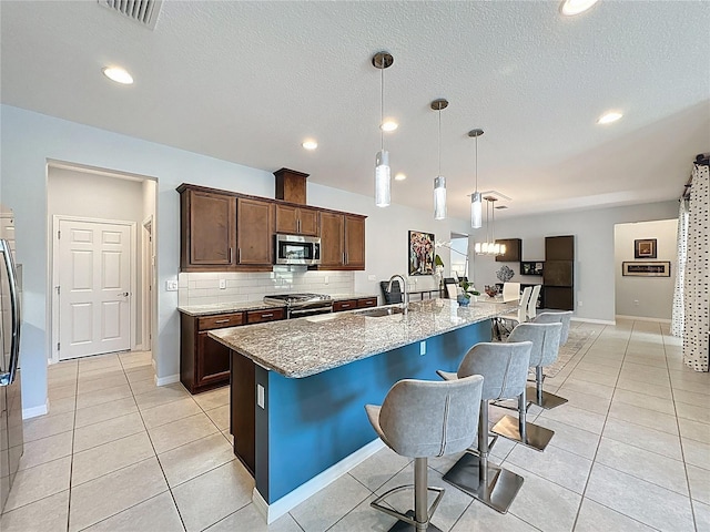 kitchen featuring a sink, a kitchen breakfast bar, tasteful backsplash, stainless steel appliances, and light stone countertops