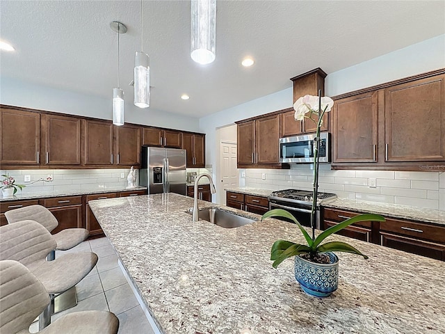 kitchen with backsplash, light stone counters, appliances with stainless steel finishes, and a sink