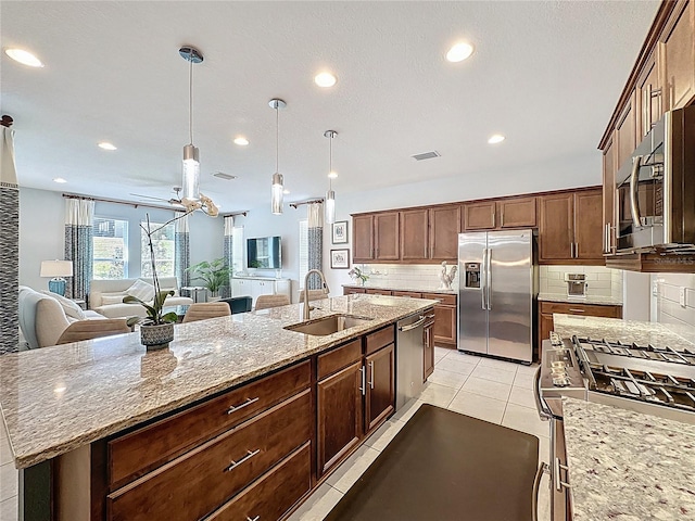 kitchen featuring visible vents, a kitchen island with sink, a sink, backsplash, and stainless steel appliances